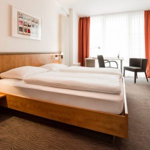 Doppelzimmer Komfort mit Doppelbett und TV im Vordergrund und Schreibtisch im Hintergrund